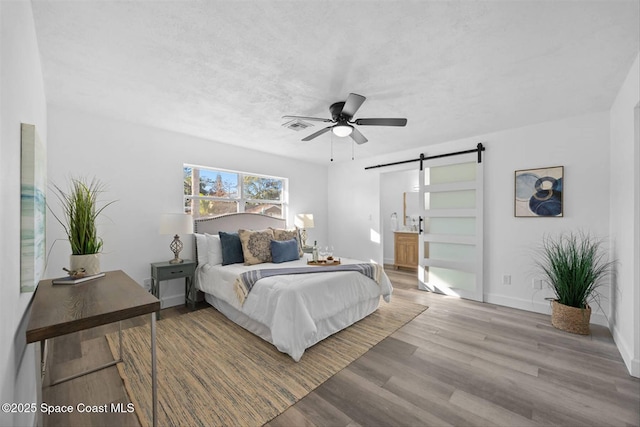 bedroom featuring ceiling fan, a barn door, ensuite bath, and hardwood / wood-style floors