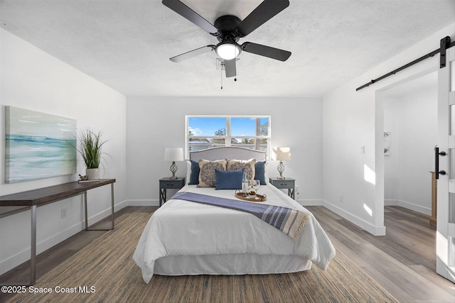 bedroom featuring ceiling fan, a barn door, and hardwood / wood-style floors