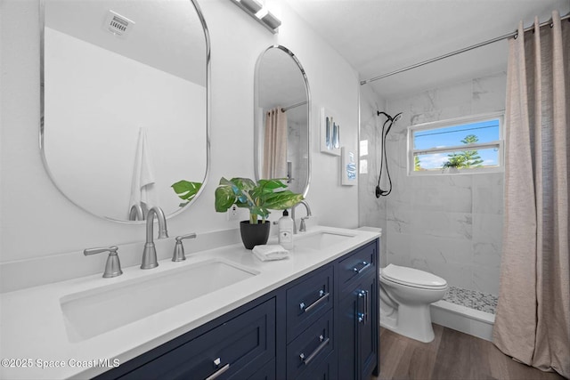 bathroom featuring wood-type flooring, toilet, vanity, and a tile shower