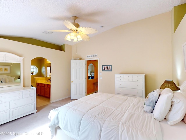 carpeted bedroom featuring ceiling fan, ensuite bathroom, vaulted ceiling, and a textured ceiling