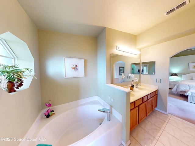 bathroom featuring a relaxing tiled tub, vanity, and tile patterned floors