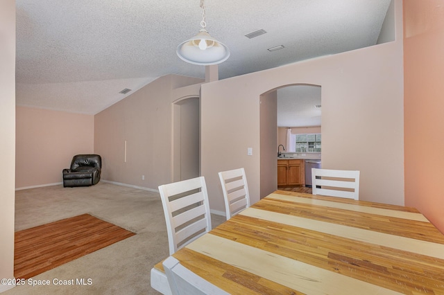 dining area with sink, light colored carpet, and a textured ceiling