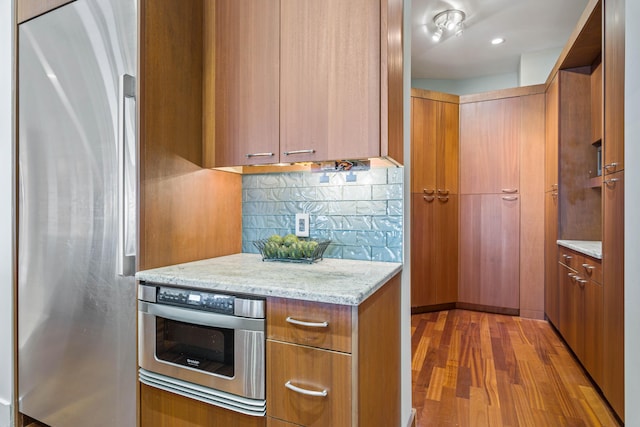 kitchen featuring tasteful backsplash, light wood-type flooring, light stone countertops, and stainless steel appliances