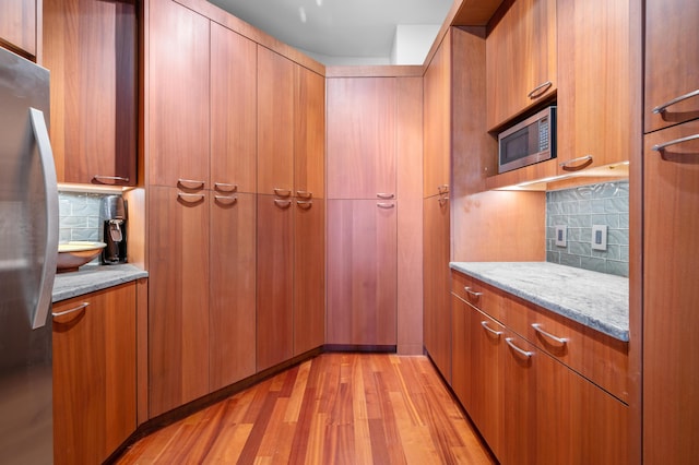 kitchen featuring light stone countertops, appliances with stainless steel finishes, light hardwood / wood-style flooring, and tasteful backsplash