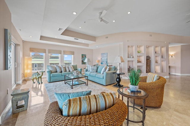 living room with ceiling fan, built in shelves, and a tray ceiling