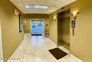 corridor with tile patterned flooring, a drop ceiling, and elevator