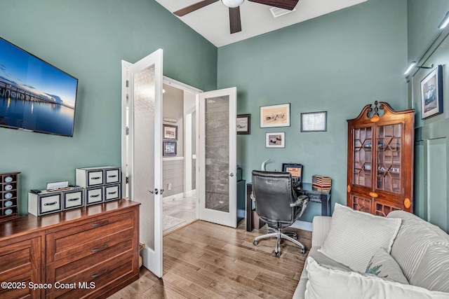 office area with a towering ceiling, light hardwood / wood-style floors, french doors, and ceiling fan