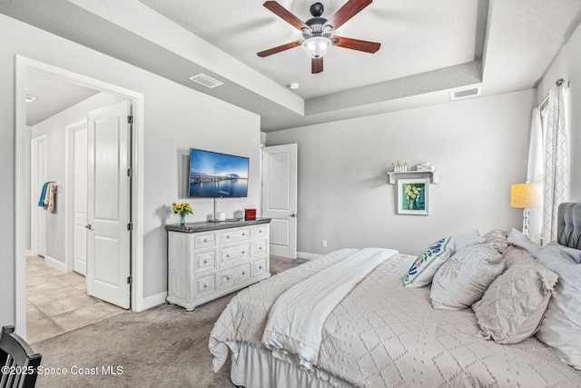 bedroom featuring light carpet, ceiling fan, and a tray ceiling