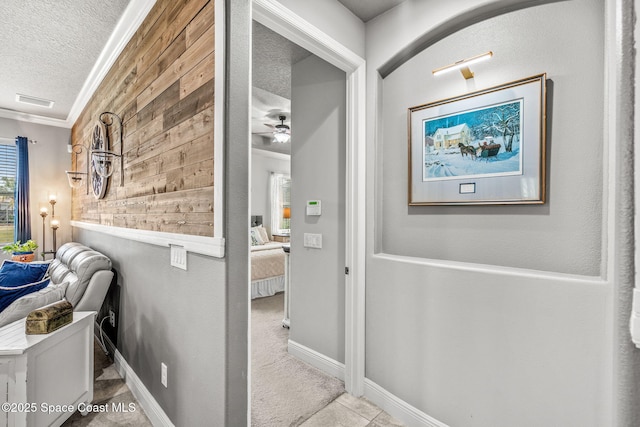 hall featuring light colored carpet, wooden walls, ornamental molding, and a textured ceiling