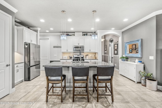 kitchen featuring a kitchen island with sink, white cabinetry, stainless steel appliances, and dark stone countertops