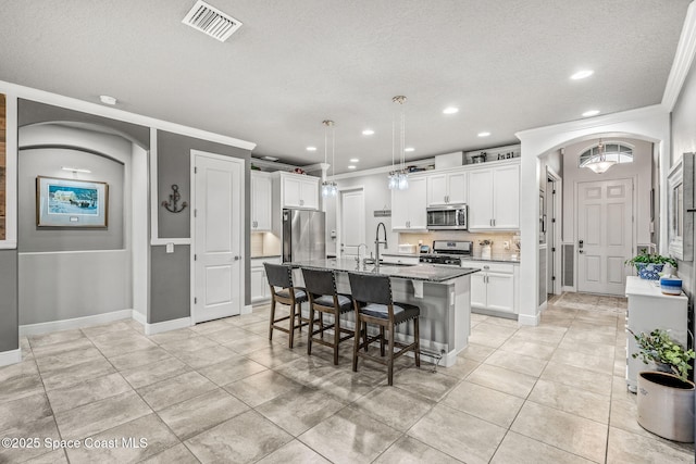 kitchen featuring stone counters, white cabinetry, sink, stainless steel appliances, and a center island with sink