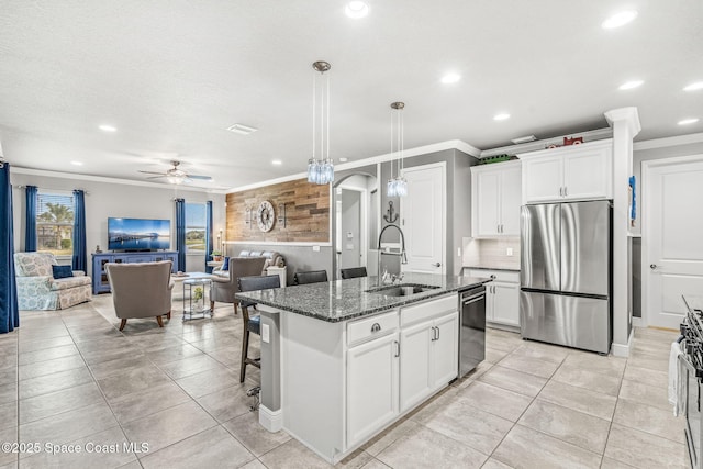 kitchen with sink, appliances with stainless steel finishes, dark stone countertops, an island with sink, and white cabinets