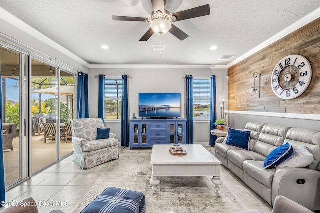 tiled living room with ceiling fan, ornamental molding, wooden walls, and a textured ceiling