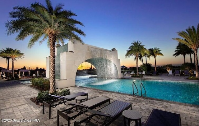 pool at dusk featuring pool water feature and a patio