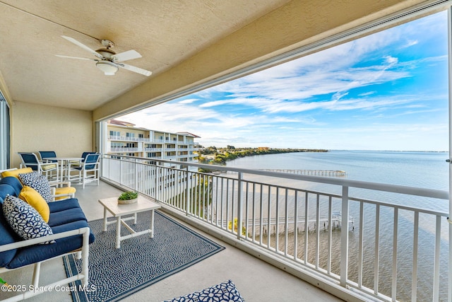 balcony with an outdoor living space, ceiling fan, and a water view