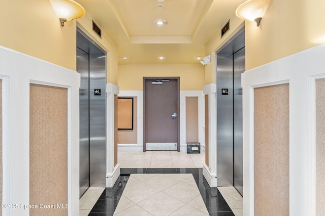 hallway with elevator, a raised ceiling, and light tile patterned floors