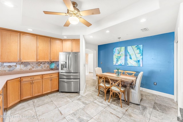 kitchen with stainless steel refrigerator with ice dispenser, hanging light fixtures, a tray ceiling, ceiling fan, and backsplash