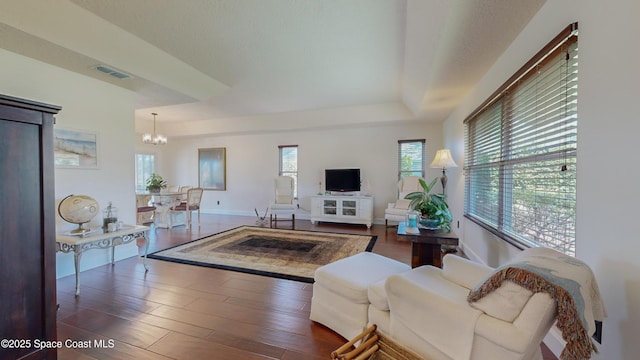 living room featuring an inviting chandelier, a healthy amount of sunlight, a raised ceiling, and dark hardwood / wood-style floors