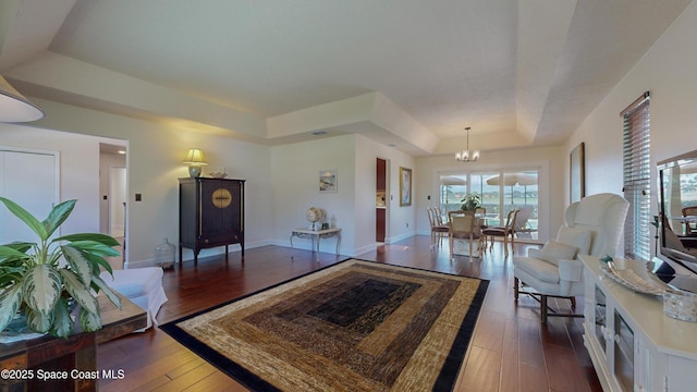 living room featuring dark wood-type flooring, a chandelier, and a raised ceiling