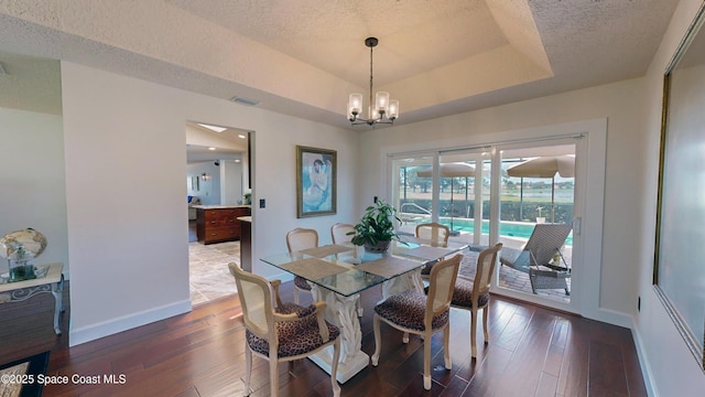 dining space with a textured ceiling, an inviting chandelier, dark hardwood / wood-style flooring, and a raised ceiling