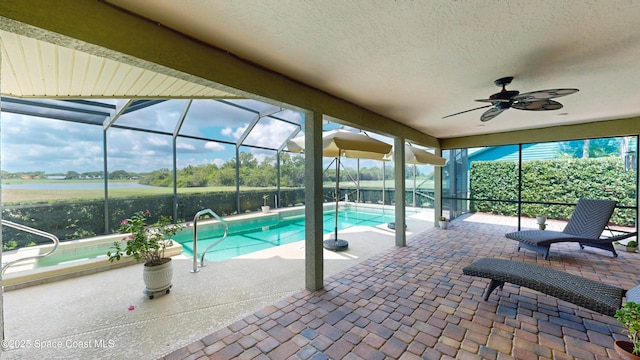 view of swimming pool featuring a water view, ceiling fan, a patio area, and a lanai