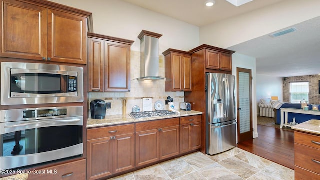 kitchen featuring light stone counters, wall chimney range hood, decorative backsplash, and stainless steel appliances