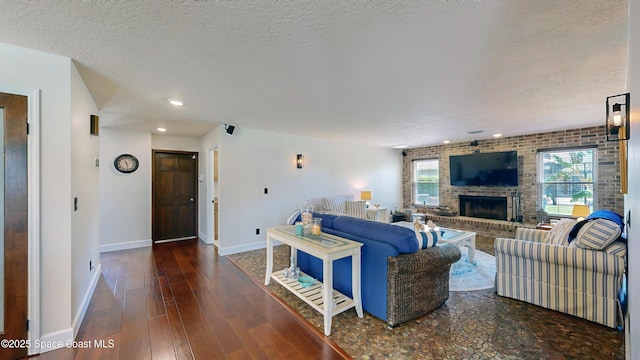 living room featuring dark wood-type flooring, a brick fireplace, brick wall, and a textured ceiling