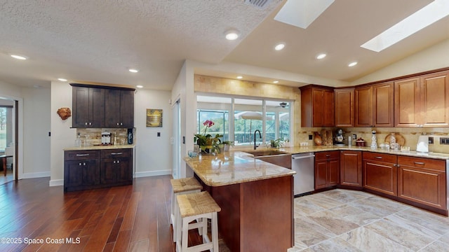 kitchen with vaulted ceiling with skylight, backsplash, kitchen peninsula, a breakfast bar, and stainless steel dishwasher