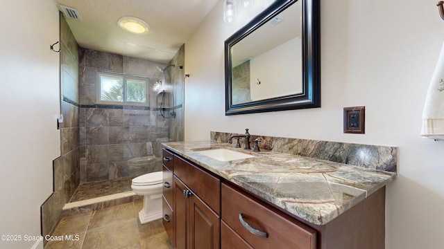 bathroom with toilet, vanity, and a tile shower