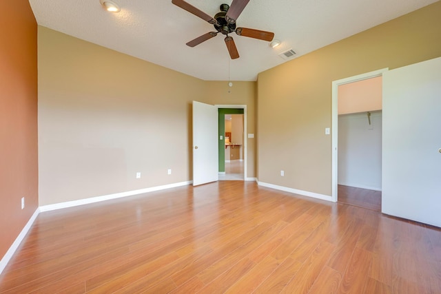 unfurnished bedroom with ceiling fan, light wood-type flooring, a textured ceiling, a walk in closet, and a closet