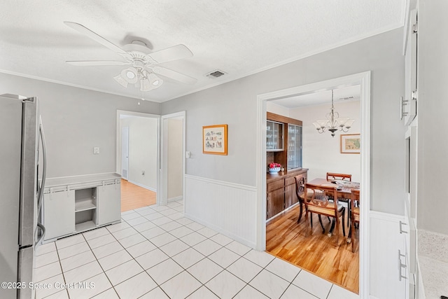 kitchen with stainless steel refrigerator, a textured ceiling, ornamental molding, light tile patterned floors, and ceiling fan with notable chandelier