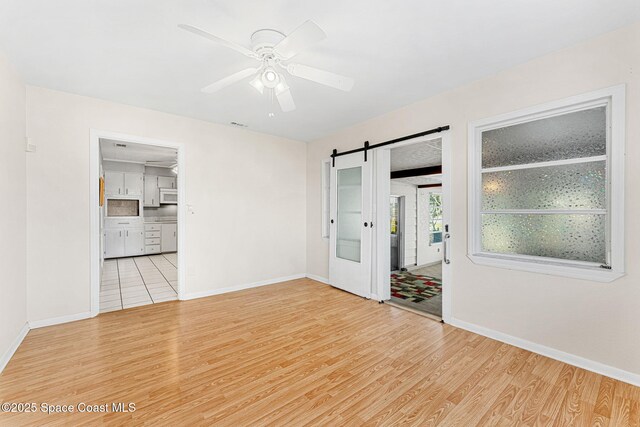 spare room featuring ceiling fan, a barn door, and light wood-type flooring