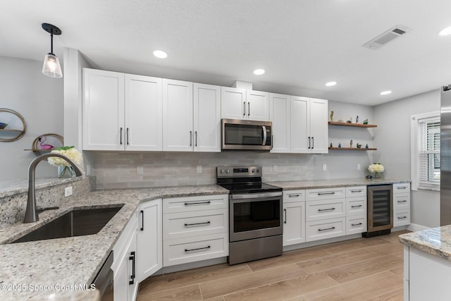 kitchen featuring white cabinetry, stainless steel appliances, decorative light fixtures, beverage cooler, and sink