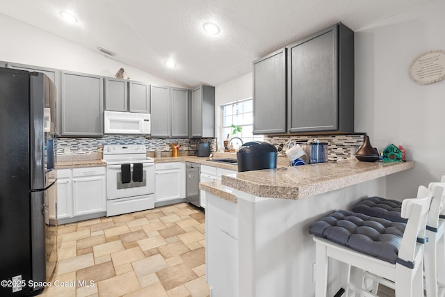 kitchen featuring white appliances, gray cabinets, kitchen peninsula, vaulted ceiling, and a breakfast bar area