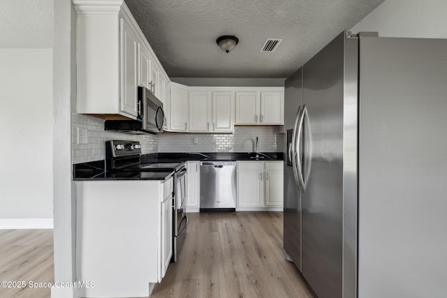 kitchen featuring a textured ceiling, appliances with stainless steel finishes, light hardwood / wood-style floors, and white cabinetry