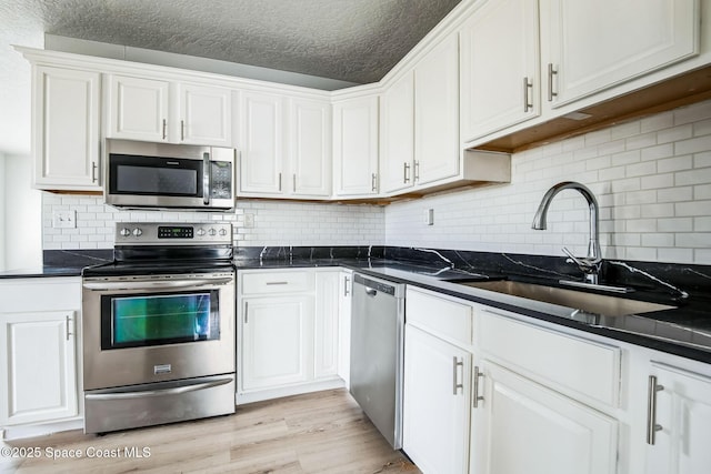 kitchen with appliances with stainless steel finishes, white cabinets, tasteful backsplash, and sink