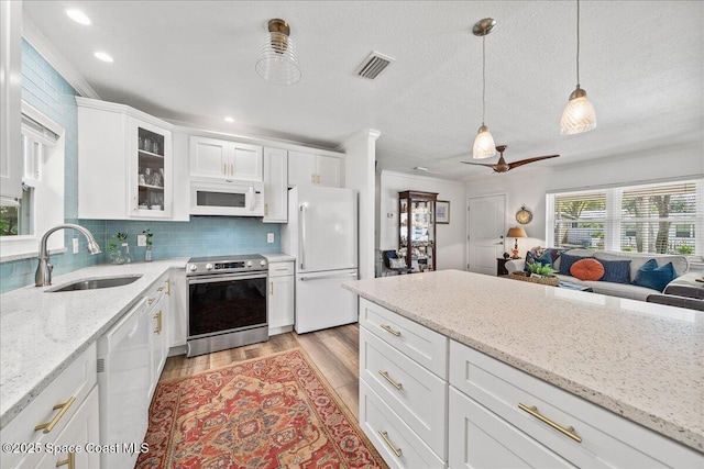 kitchen with pendant lighting, sink, white appliances, light stone counters, and white cabinets