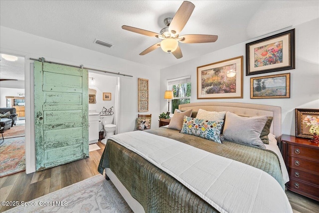 bedroom with ensuite bath, ceiling fan, hardwood / wood-style floors, a textured ceiling, and a barn door