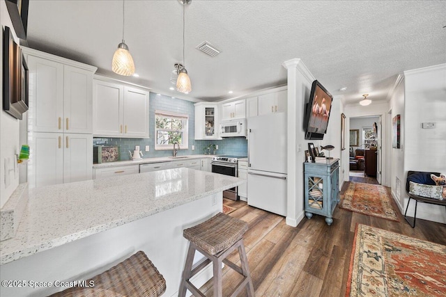 kitchen with white cabinetry, a breakfast bar, white appliances, and decorative light fixtures