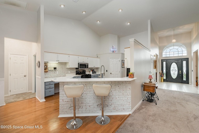 kitchen with black gas stove, white cabinets, a breakfast bar, high vaulted ceiling, and decorative backsplash