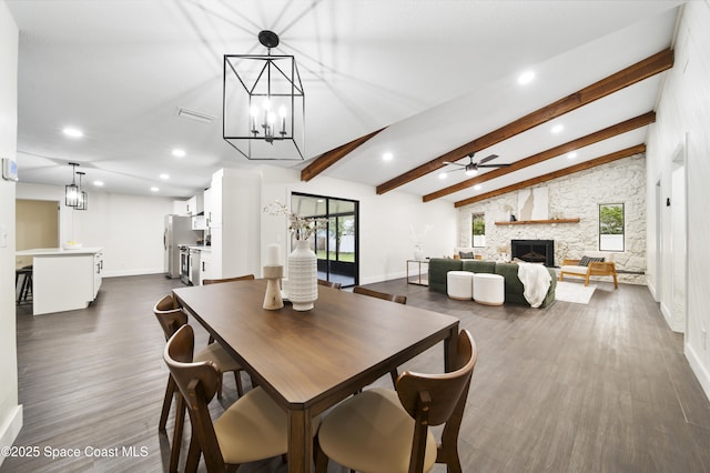 dining space with ceiling fan, lofted ceiling with beams, dark hardwood / wood-style flooring, and a stone fireplace