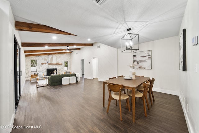 dining space featuring dark hardwood / wood-style floors, lofted ceiling with beams, a stone fireplace, a textured ceiling, and ceiling fan with notable chandelier