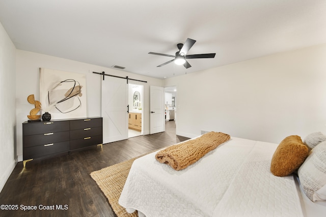 bedroom featuring ceiling fan, dark hardwood / wood-style flooring, ensuite bath, and a barn door