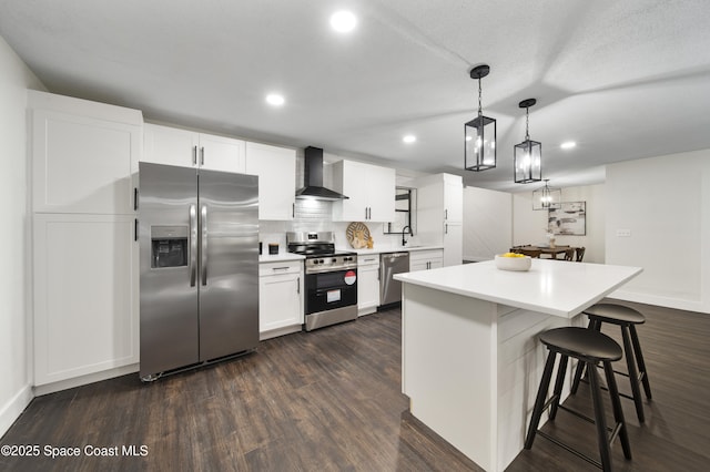 kitchen featuring white cabinetry, stainless steel appliances, tasteful backsplash, wall chimney range hood, and pendant lighting