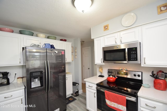 kitchen featuring a textured ceiling, appliances with stainless steel finishes, light hardwood / wood-style floors, and white cabinetry