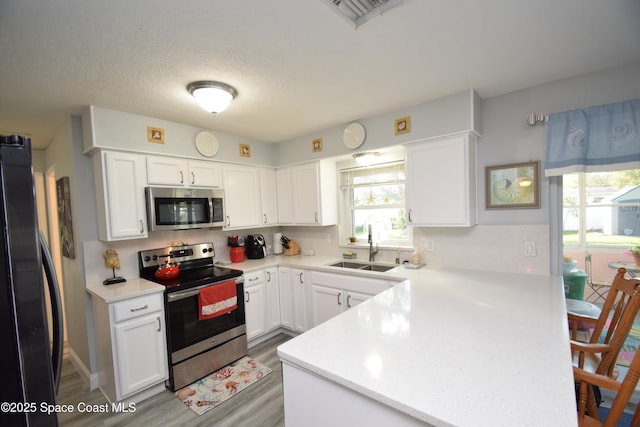 kitchen featuring a textured ceiling, white cabinets, appliances with stainless steel finishes, light hardwood / wood-style floors, and sink