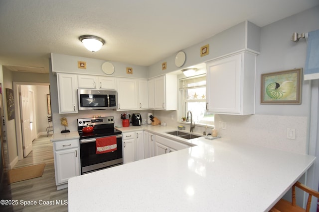 kitchen with white cabinetry, kitchen peninsula, stainless steel appliances, light wood-type flooring, and sink