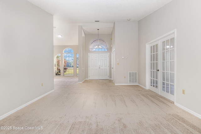 entrance foyer with a towering ceiling, light colored carpet, french doors, and a notable chandelier