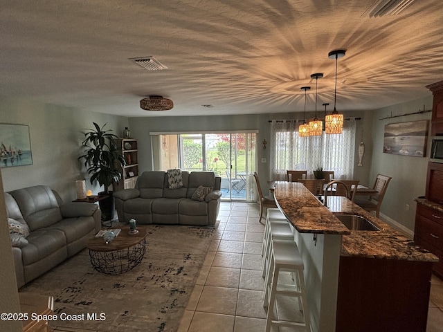 living room with sink, light tile patterned floors, a notable chandelier, and a textured ceiling