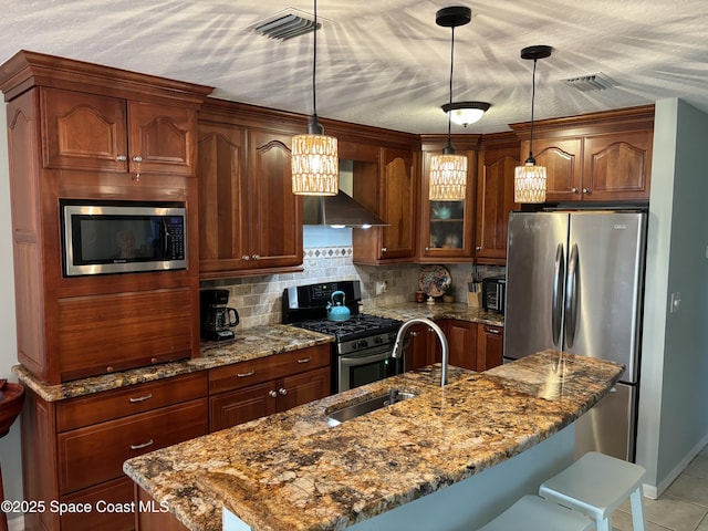 kitchen featuring sink, hanging light fixtures, appliances with stainless steel finishes, an island with sink, and stone counters